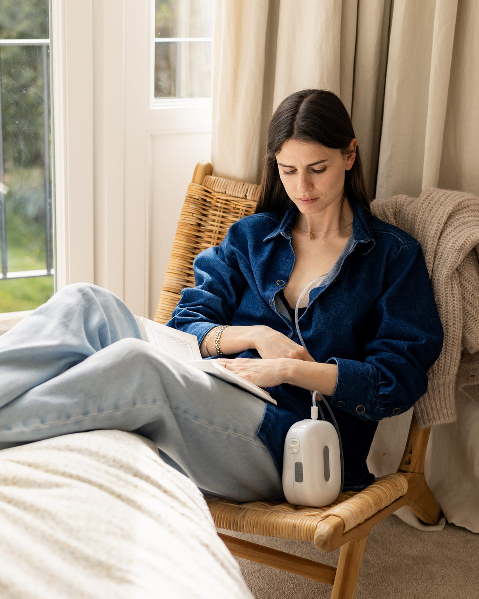 A mother reads in an armchair while the Lileo breast pump is running.