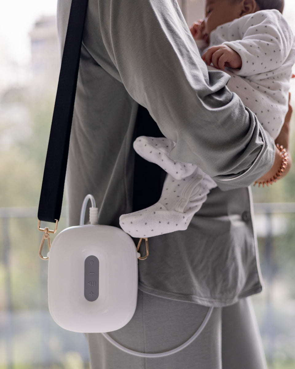 A mother holds her baby, the Lileo breast pump worn across the body like a handbag.