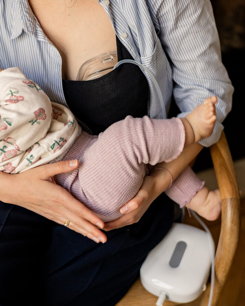 A mother pumps her milk with the Lileo breast pump, her baby on her lap.